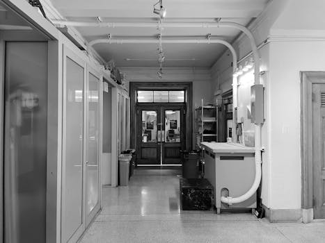 Black and white photo of an empty industrial hallway with pipes and cabinets.